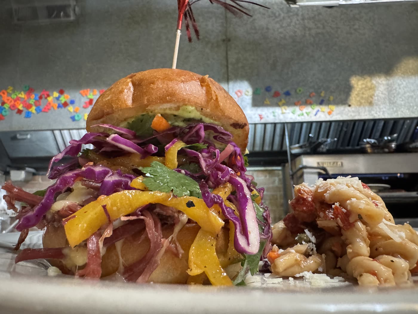 Sammy piled high with shaved meat, purple slaw, yellow peppers and cilantro on a brioche bun, with pasta salad